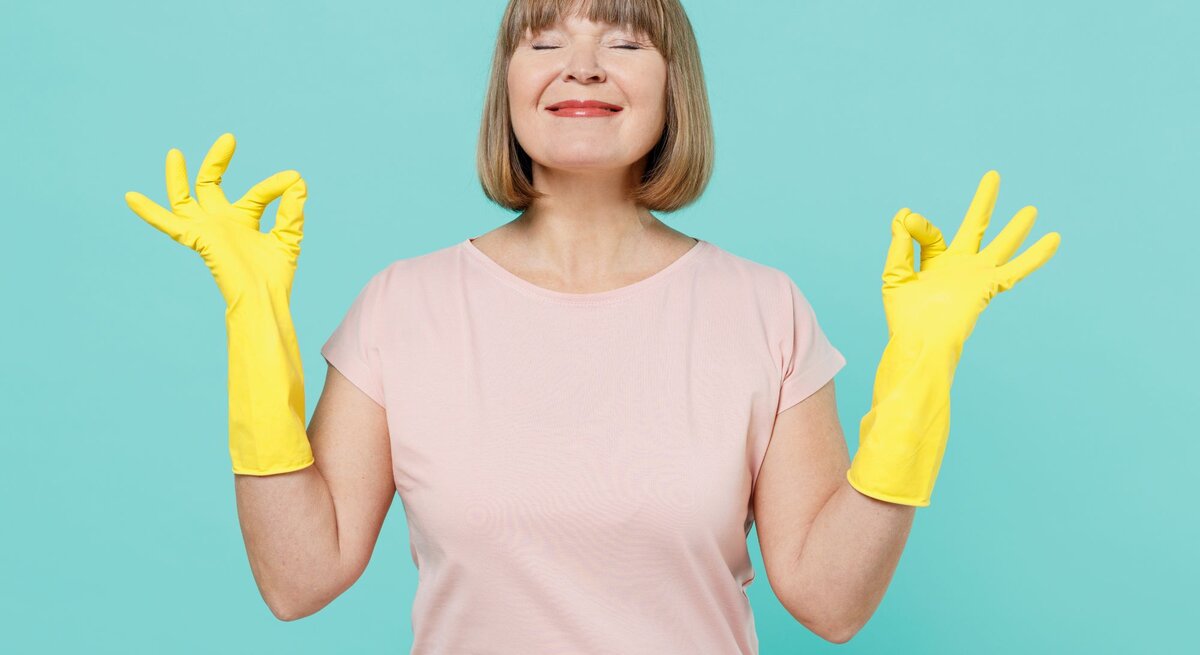 Eine Frau trägt gelbe Gummihandschuhe, hält beide Hände im "OK"-Zeichen und steht vor einem türkisfarbenen Hintergrund.