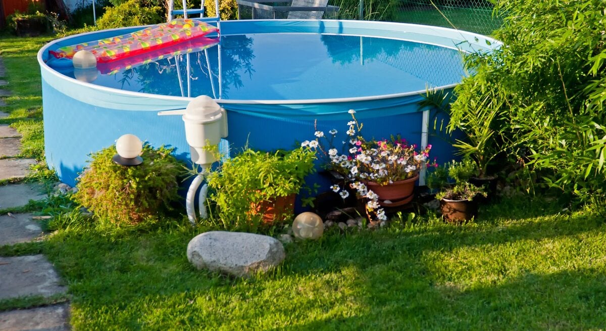 Ein gepflegter Garten mit frisch gemähtem Rasen, blühenden Pflanzen und einem runden Pool, in dem sich die Umgebung spiegelt.
