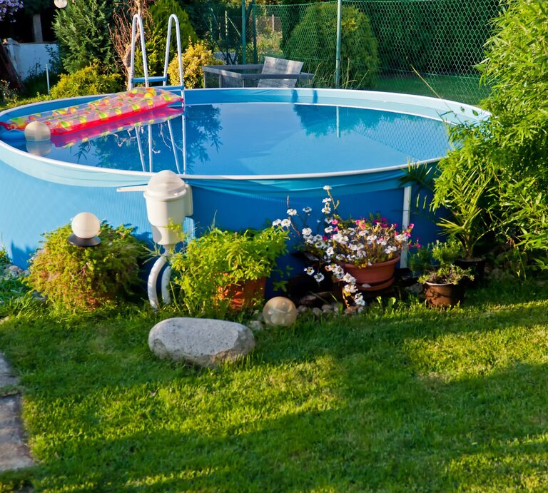 Ein gepflegter Garten mit frisch gemähtem Rasen, blühenden Pflanzen und einem runden Pool, in dem sich die Umgebung spiegelt. | © Adobe Stock/ Jan S.
