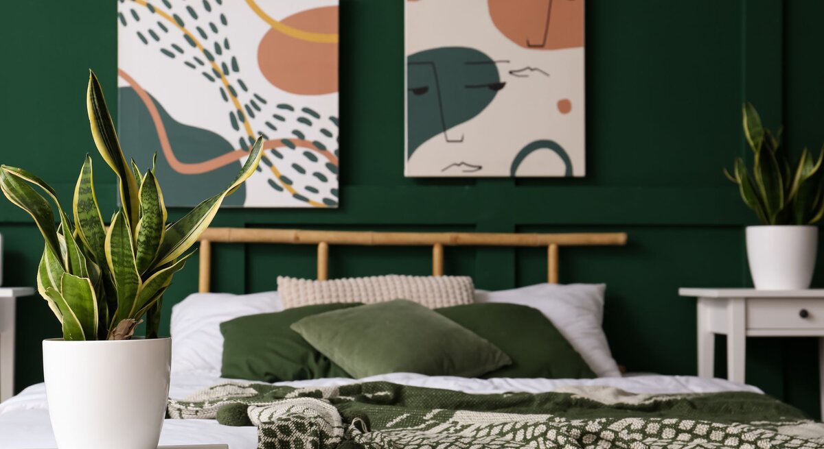 Modern eingerichtetes Schlafzimmer mit grünem Wandanstrich, Pflanzen in weißen Töpfen und abstrakter Kunst über dem Bett.
