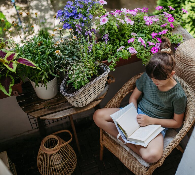 Zu sehen ist eine Frau, die auf ihrem Balkon entspannt, der voller Pflanzen ist. | © GettyImages/Halfpoint Images