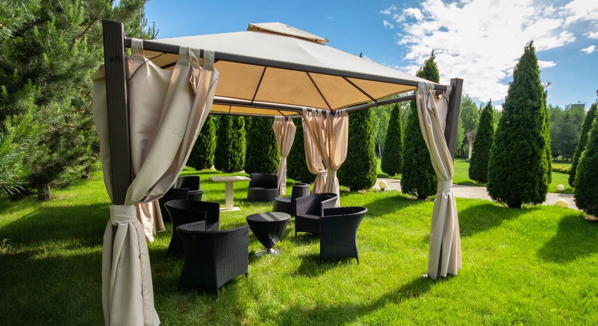Ein luftiger Gartenpavillon mit offenen Vorhängen lädt inmitten symmetrisch gepflanzter Koniferen zum Verweilen ein.