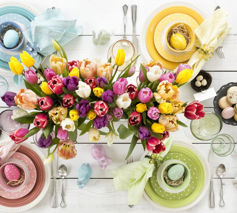Bunte Tulpen in Gelb, Rot, Rosa und Lila schmücken eine festlich gedeckte Ostertafel mit pastellfarbenem Geschirr und verzierten Ostereiern. | © GettyImages/Liliboas