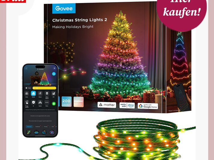 Bunter Weihnachtsbaum mit LED-Lichterkette in Regenbogenfarben, umgeben von Geschenken, Smartphone-App zur Steuerung im Vordergrund. | © Govee / bildderfrau.de