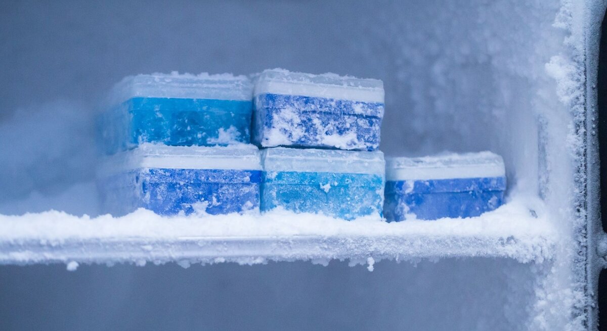 Im frostigen Inneren eines Gefrierschranks liegen übereinander gestapelte, vereiste blaue Kühlakkus.