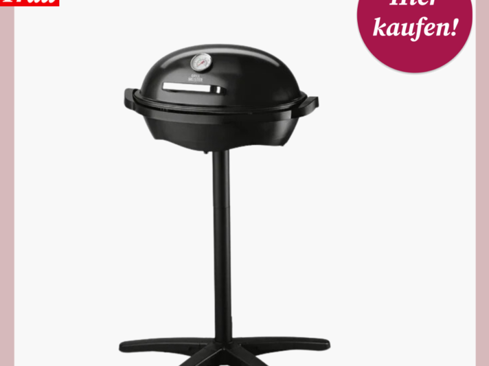 Ein schwarzer Elektrogrill auf einem Stativ mit einer großen, runden Basis und einer Kuppelhaube mit eingebautem Thermometer. Über dem Bild befindet sich ein Logo mit der Aufschrift "Bild der Frau" in Weiß auf einem roten Hintergrund, und in der rechten oberen Ecke befindet sich ein kreisförmiges, magentafarbenes Etikett mit der weißen Aufschrift "Hier kaufen!". Der Hintergrund ist einfarbig hellrosa. | © Lidl 