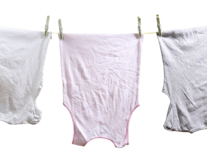 Drei vergilbte Wäschestücke, die an einer Wäscheleine hängen. In der Mitte befindet sich ein rosa Unterhemd, flankiert von zwei weißen Unterhemden, die jeweils mit grünen Wäscheklammern befestigt sind. | © iStock.com / MediaProduction