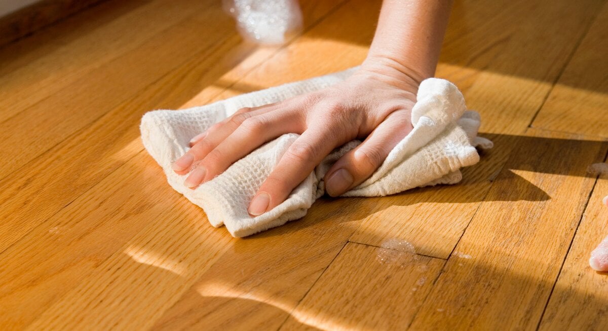Hand mit Lappen beim Parkett reinigen
