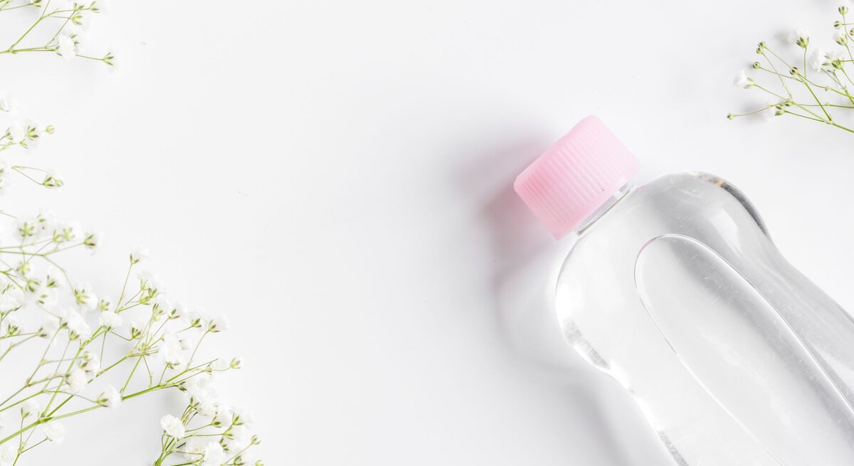 Eine transparente Flasche mit rosa Schraubverschluss liegt auf weißem Untergrund, umgeben von filigranen weißen Blüten.
