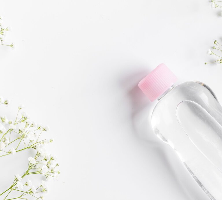 Eine transparente Flasche mit rosa Schraubverschluss liegt auf weißem Untergrund, umgeben von filigranen weißen Blüten. | © Adobe Stock/279photo