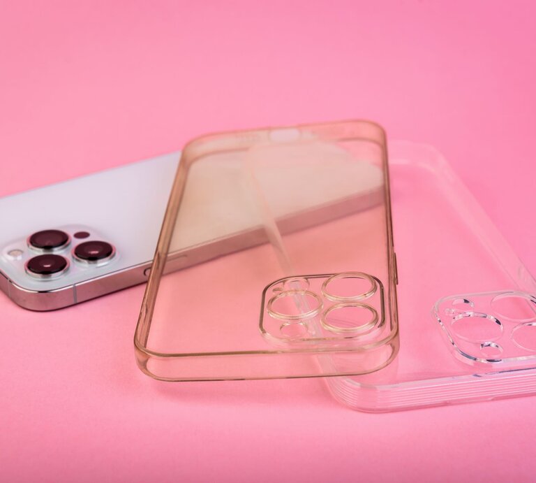 Eine silberne Smartphone-Rückseite mit drei Kameralinsen liegt auf rosa Hintergrund, daneben zwei transparente Handyhüllen, eine davon ist vergilbt. | © Adobe Stock/Natallia