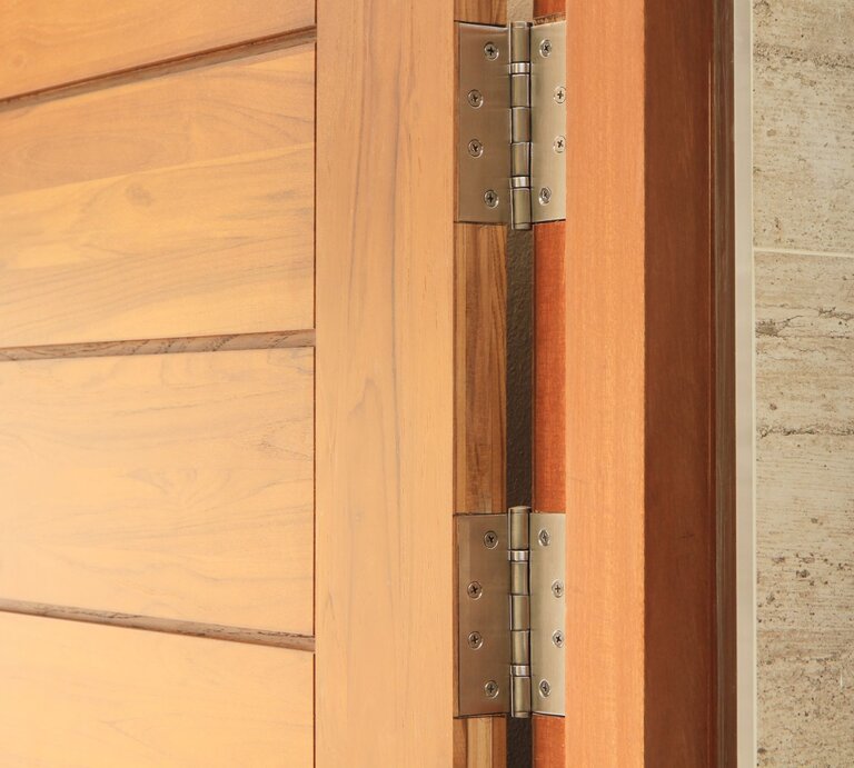 Holztür mit sichtbarem Metallscharnier, das an einer beige gekachelten Wand montiert ist. | © iStock.com/drpnncpp