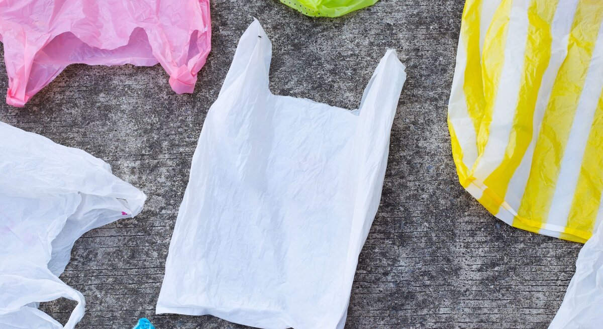Mehrere Plastiktragetaschen in verschiedenen Farben liegen auf einem grauen Untergrund.