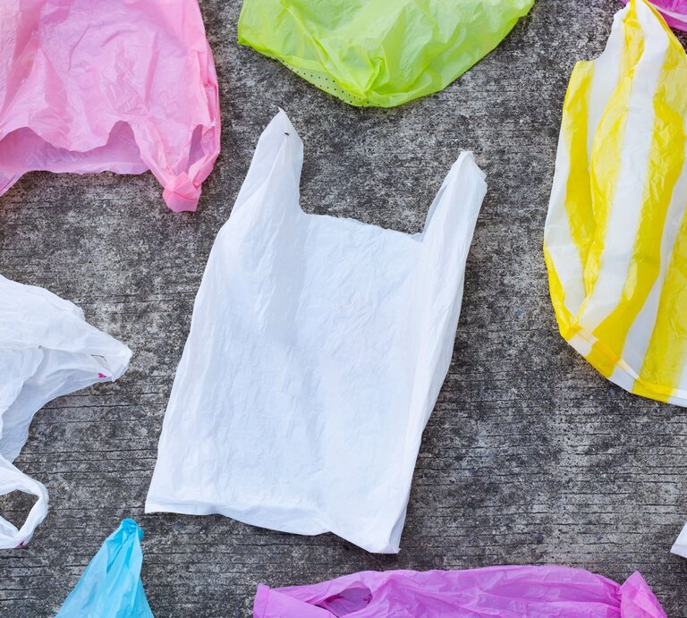 Mehrere Plastiktragetaschen in verschiedenen Farben liegen auf einem grauen Untergrund. | © Getty Images/Bowonpat Sakaew / EyeEm