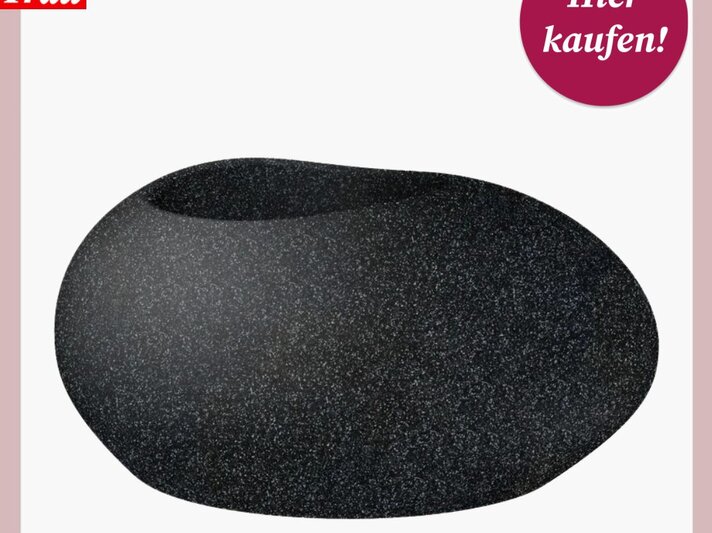 Ein schwarzes Pflanzgefäß mit einer glatten, abgerundeten und asymmetrischen Form, die an einen flachen, übergroßen Kieselstein erinnert. Der Topf hat eine raue, texturierte Oberfläche, die Stein ähnelt. Im oberen Bereich befindet sich eine ovale Öffnung für Pflanzen. In der oberen rechten Ecke ist ein rosa Kreis mit dem Text "Hier kaufen!" darüber, und in der oberen linken Ecke das Logo "Bild der Frau" auf einem weißen Hintergrund. | © Lidl