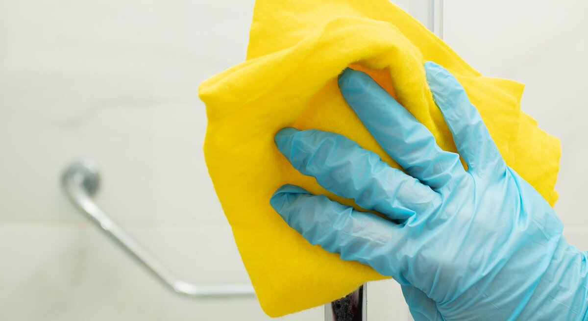 Hand in blauem Putzhandschuh und gelber Putzlappen