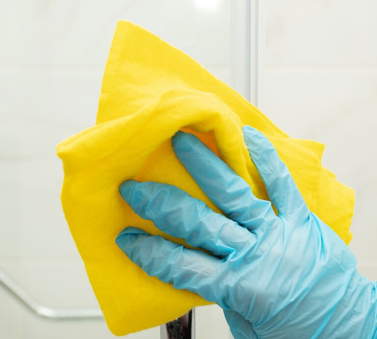 Hand in blauem Putzhandschuh und gelber Putzlappen | © Adobe Stock