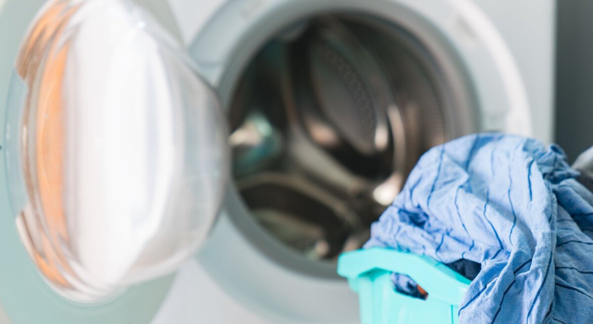 Geöffnete Waschmaschine mit frischer Wäsche neben voller blauer Wäschekorb.