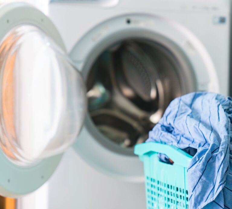 Geöffnete Waschmaschine mit frischer Wäsche neben voller blauer Wäschekorb. | © Gettyimages/chanakon laorob