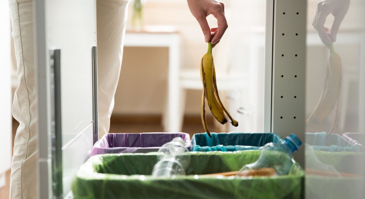 Eine Hand wirft eine Bananenschale in einen geöffneten Küchenmülleimer.