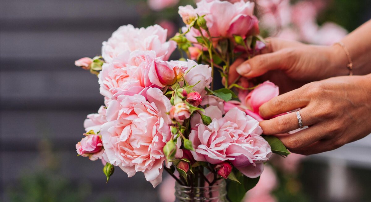 Eine Frau drapiert Rosen in einer Vase draußen. 