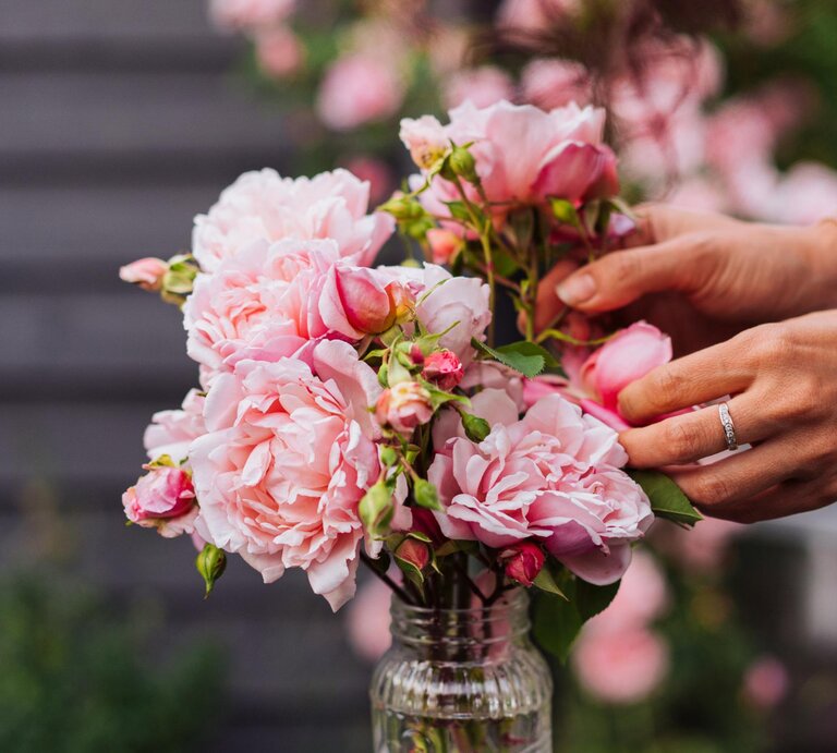 Eine Frau drapiert Rosen in einer Vase draußen.  | © Getty Images