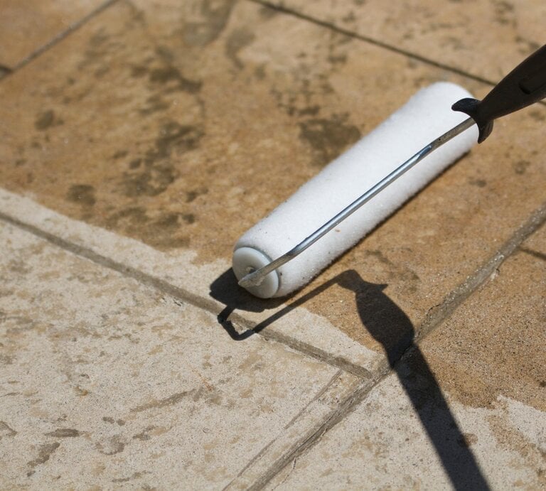 Jemand trägt eine Versiegelung auf Terrassenplatten mit einer Rolle auf.  | © Getty Images