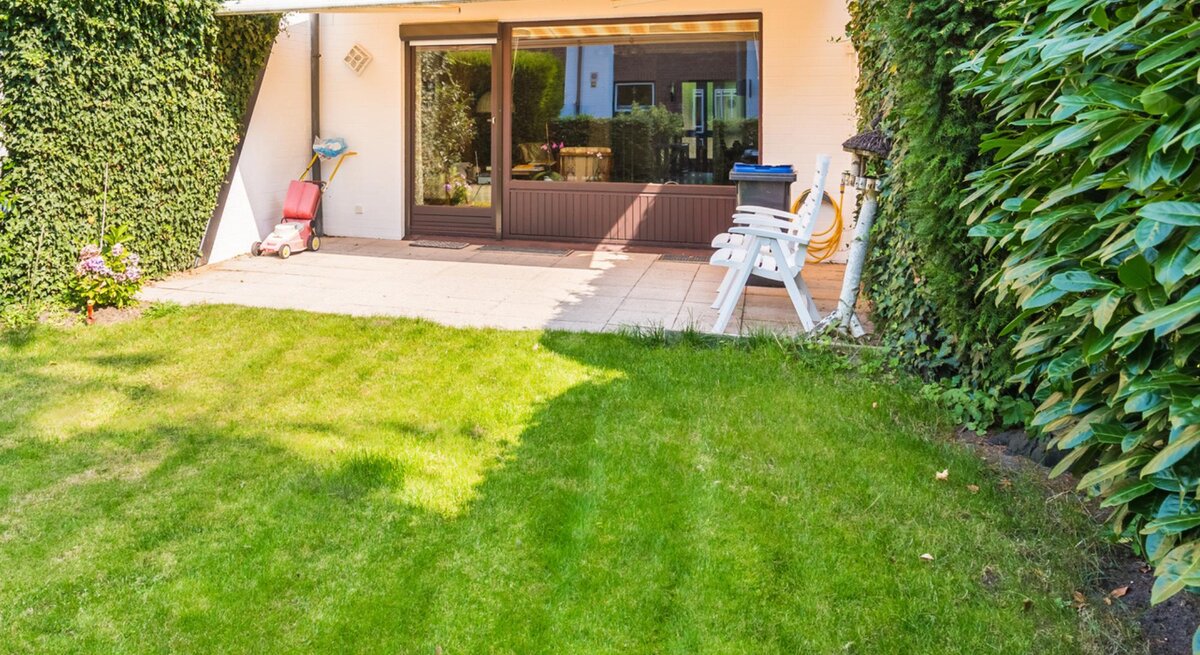 Terrasse und Garten von einem älteren Reihenhaus mit einer Hecke links und rechts zu den Nachbarn. 