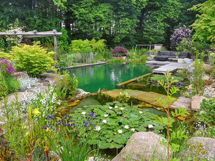 Üppiger Garten mit Natur-Schwimmteich, Seerosen und Holzdeck samt Lounge, umgeben von Stauden und Gehölzen. | © Callwey Verlag/ Galabau Kreye