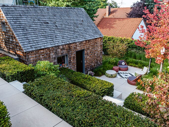 Tiefergelegter Gartenhof mit schindelverkleidetem Häuschen, streng geschnittenen Hecken und moderner Sitzgruppe zwischen herbstlich gefärbten Bäumen. | © Callwey Verlag/ Ferdinand Graf Luckner