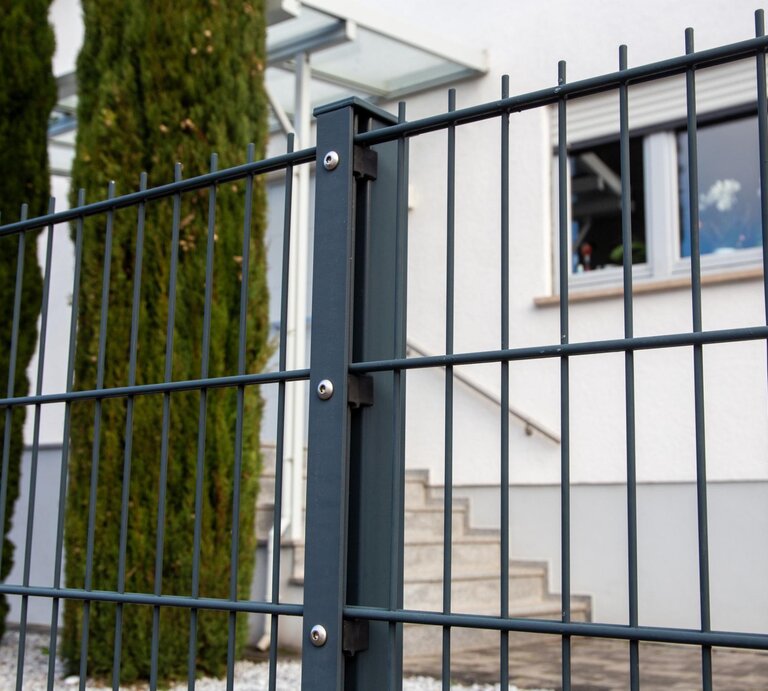 Stabmattenzaun in Nahaufnahme. Dahinter Bäume und ein Haus.  | © Getty Images