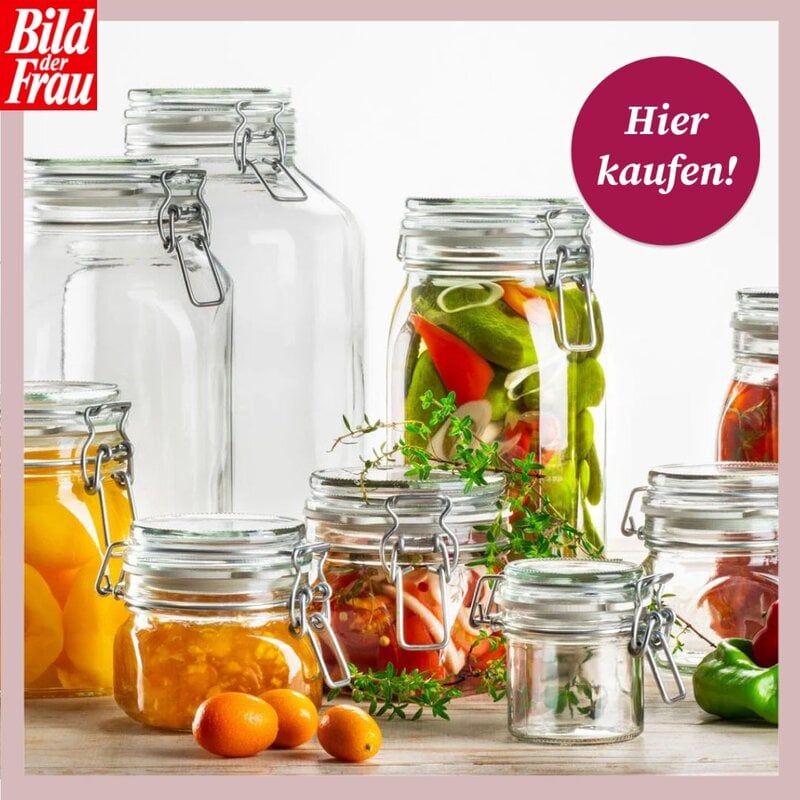 Sammlung von Bügelgläsern in verschiedenen Größen auf Holzfläche; einige leer, andere gefüllt (z.B. Gurken mit Paprika und Zwiebeln, gelbe und orange Marmeladen, frische Kräuter und Zitrusfrüchte davor). Oben links das „Bild der Frau“-Logo, oben rechts ein runder Magenta-Störer mit „Hier kaufen!“, roséfarbener Rand. | © Lidl