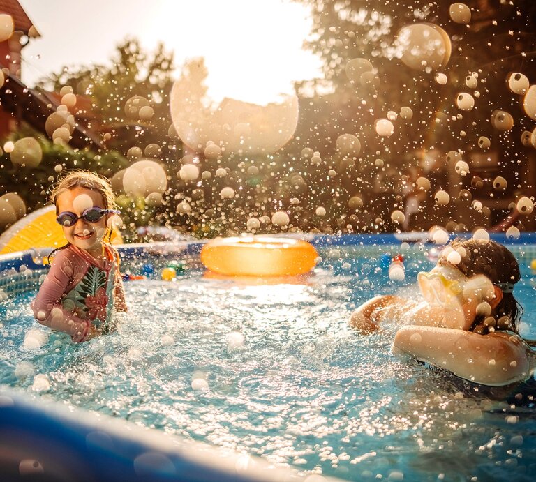 Zwei Kinder planschen und spielen mit Schwimmbrillen in einem Gartenpool an einem sonnigen Sommertag. | © GettyImages/enigma_images