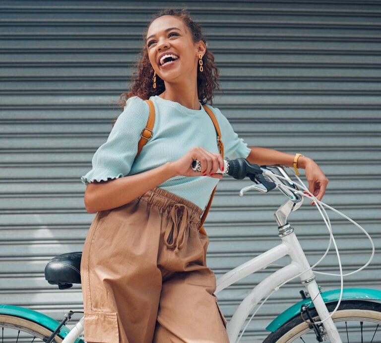 Junge, lächelnde Frau schiebt ein Fahrrad | © Getty Images