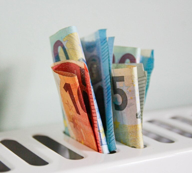 Mehrere gefaltete Euro-Banknoten ragen aus den Schlitzen eines weißen Toasters vor hellem Hintergrund und symbolisieren Geldverlust. | © Getty Images