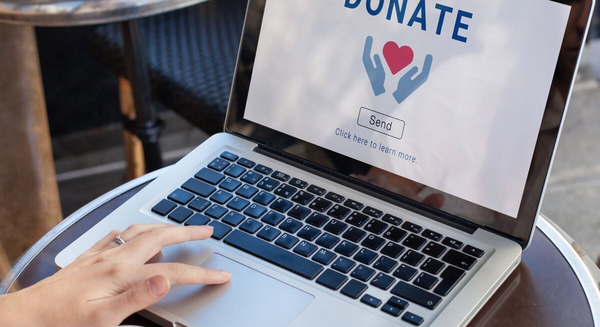 Zu sehen ist eine Laptop auf dem Donate steht und Frauenhände, die diesen bedienen.