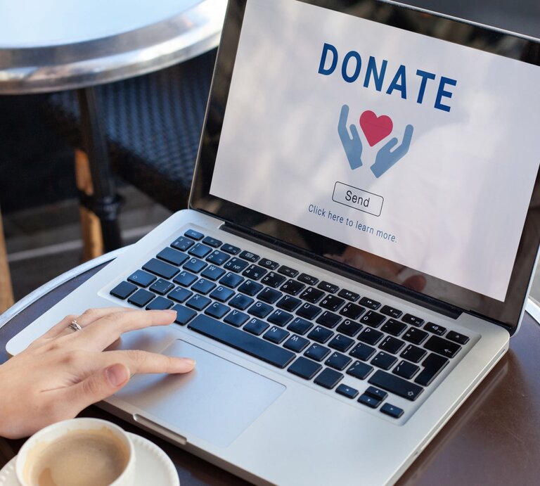 Zu sehen ist eine Laptop auf dem Donate steht und Frauenhände, die diesen bedienen. | © Shutterstock/Song_about_summer