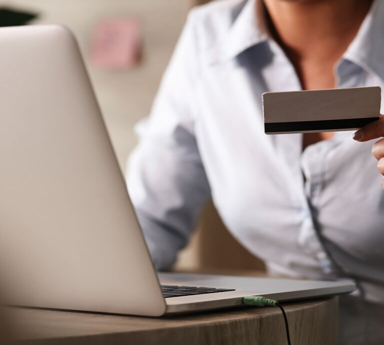 Zu sehen ist eine Frau, die eine Kreditkarte hält und am Laptop sitzt. | © Shutterstock/ Drazen Zigic