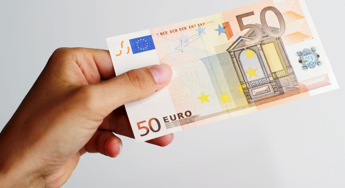 Ein 50-Euro-Schein wird von einer Hand mit leicht gebogenen Fingern gehalten, vor einem schlichten weißen Hintergrund.