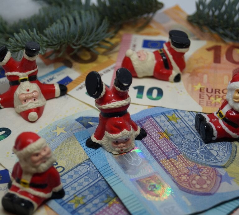 Zu sehen sind Weihnachtsmänner, die auf Geld tanzen | © Shutterstock/ Steidi