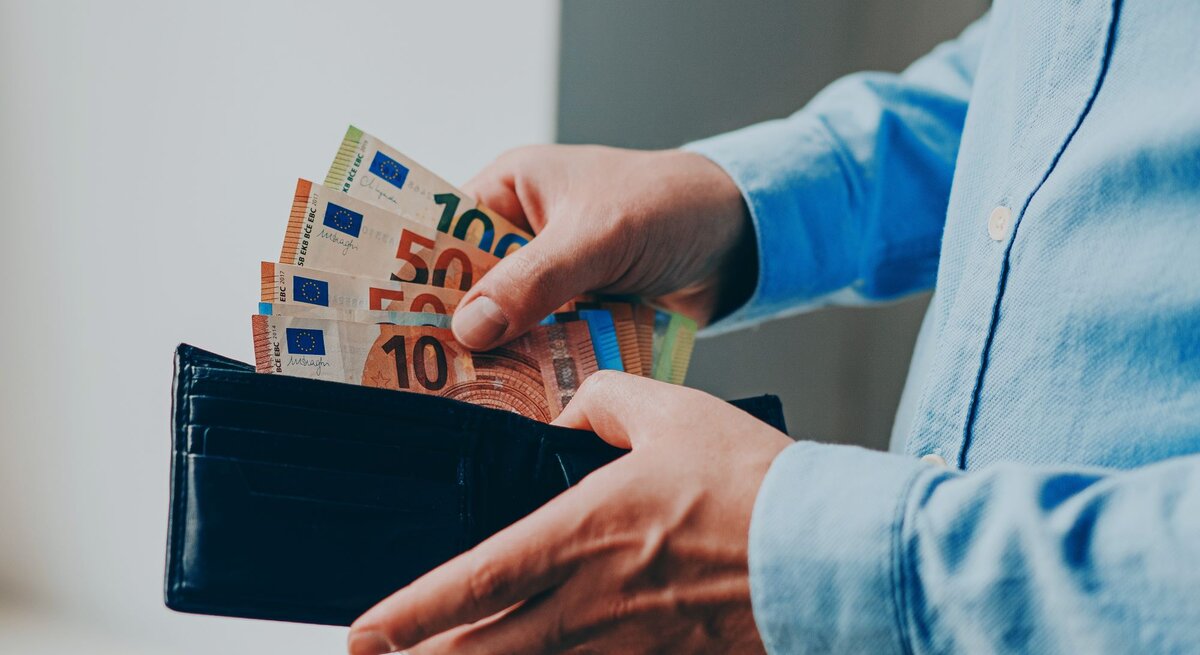 Zu sehen ist eine Hand, die Geld in ein Portemonnaie steckt.