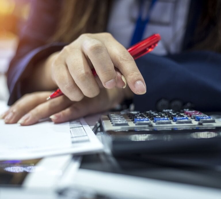 Zu sehen ist eine Frauenhand am Taschenrechner | © GettyImages/	Virojt Changyencham