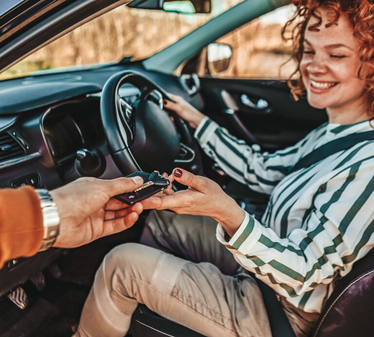Frau sitzt lächeln im Auto, geöffnete Tür und bekommt den Schlüssel gereicht. | © gettyimages/	ljubaphoto