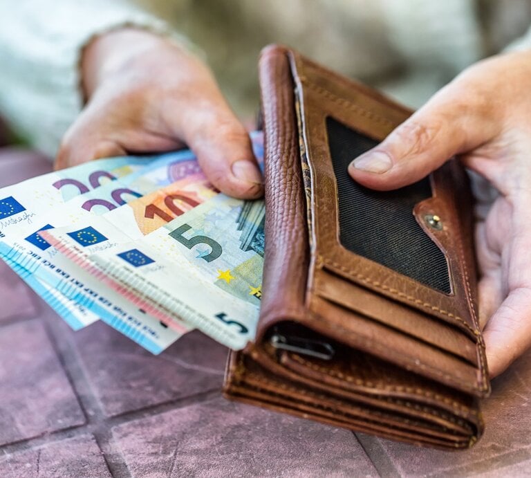 Eine Nahaufnahme von zwei Händen, die ein braunes Lederportemonnaie halten, aus dem mehrere Euro-Banknoten herausragen, darunter Scheine mit den Werten 5, 10, 20 und 50 Euro. Die Szene wirkt, als ob jemand gerade dabei ist, Geld zu zählen oder zu organisieren. | © Adobe Stock/ Extended License