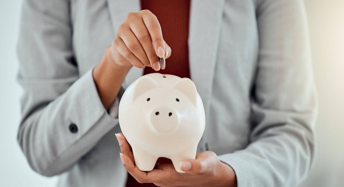 Eine Frau packt Geld in ein Sparschwein.