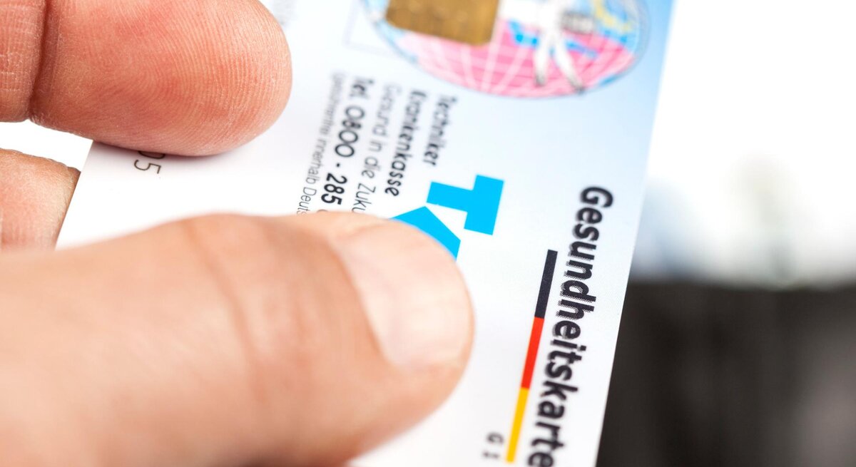 Person gibt eine Krankenkarte der Techniker Krankenversicherung einem Arzt. 