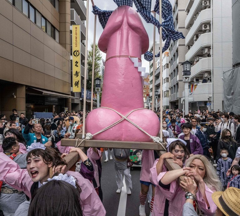 Menschen in bunten Kostümen tragen bei einem Straßenfest in Japan eine große pinke Penis-Skulptur durch eine dicht gedrängte Menge. | © Getty Images / YUICHI YAMAZAKI 