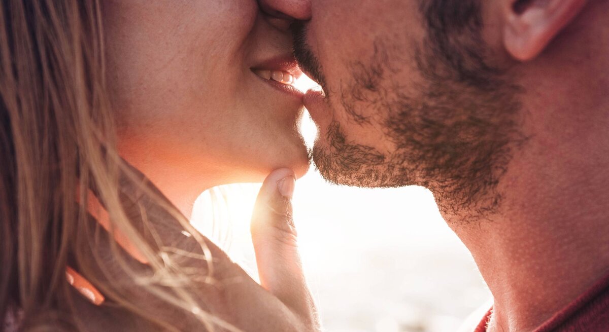 Mann und Frau küssen sich. Beide scheinen sich in einem romantischen Moment zu befinden, wobei der Mann sanft das Kinn der Frau berührt und sie sich gegenseitig sehr nahe sind.