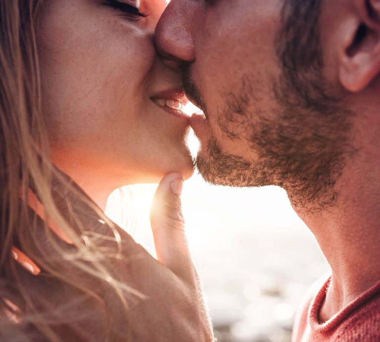 Mann und Frau küssen sich. Beide scheinen sich in einem romantischen Moment zu befinden, wobei der Mann sanft das Kinn der Frau berührt und sie sich gegenseitig sehr nahe sind. | © Adobe Stock / Davide Angelini