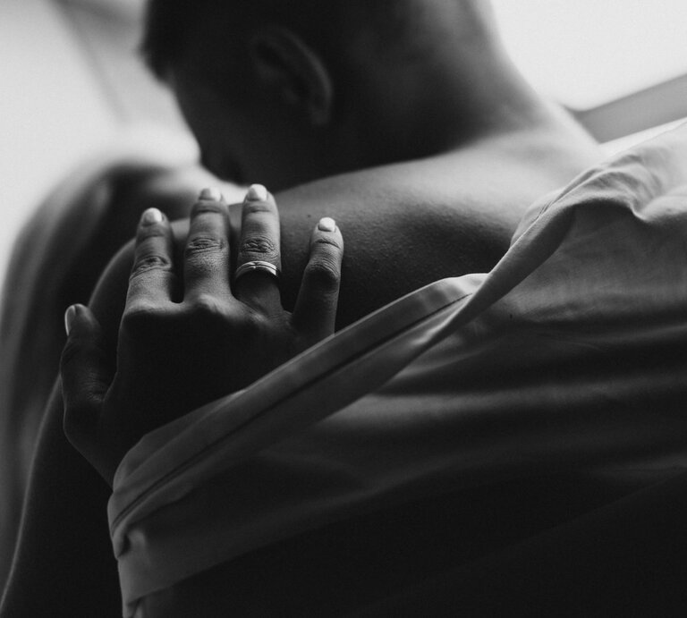 Nahaufnahme eines jungen Paares in inniger Umarmung, eine Hand mit Ring ruht zärtlich auf der nackten Schulter. | © Adobe Stock / Oksana